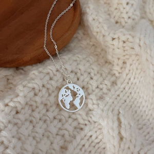 Macro shot of silver world map cutout pendant on fine chain over white sweater