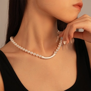 Minimalist pearl necklace with silver metal tube charm worn on neck over black top