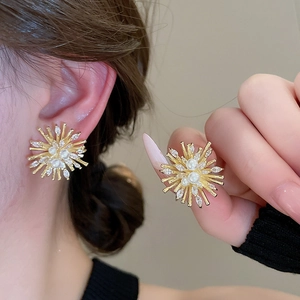 Detail of golden firework stud earrings with zircon crystals and faux pearl on model