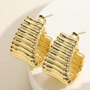Macro shot of gold wide C-shape hoop earrings with textured horizontal wave pattern