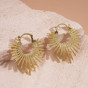 Macro detail of golden sunburst fan-shaped earrings on a beige textured stone base