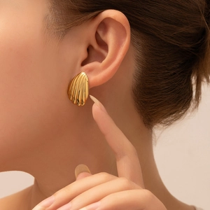 Close-up of elegant gold fan-shaped shell earrings worn by a model in a side view