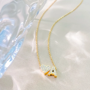 Macro detail of gold necklace featuring zircon-encrusted heart and letter A pendants