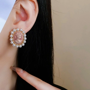 Gros plan de boucles d'oreilles camée rose vintage portées sur le lobe d'oreille