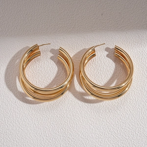 Detail view of triple-layered golden geometric C-shaped hoop earrings on textured surface