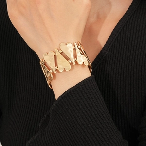 Détail d'un large bracelet cœur doré avec maillons texturés sur un tissu noir