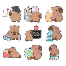 Macro detail of nine cartoon capybara enamel pins showing school and education themes