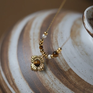 Macro shot of tiger eye sunflower pendant with gold beads and pearls for women