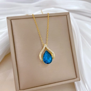 Macro detail of golden necklace featuring a blue teardrop gemstone and sparkling zircons