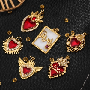 Close-up of gold-plated heart charms with red zircons and wings on black texture