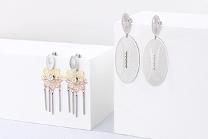 Gros plan sur boucles d'oreilles strass ajourées et clous à pompons sur présentoir blanc