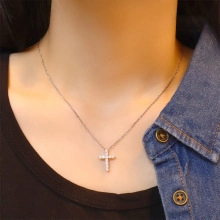 Macro detail of silver cross pendant necklace with white zircons on model neck