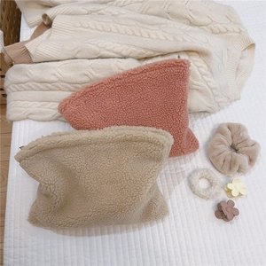 Flat lay of soft lamb wool cosmetic bags in pink and beige with plush hair accessories