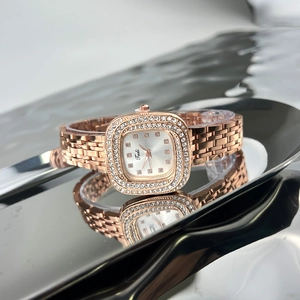 Detailed macro view of rose gold square watch with crystal bezel on reflective silver tray