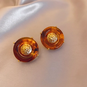 Close-up of vintage round amber stud earrings with golden flower detail and silk background