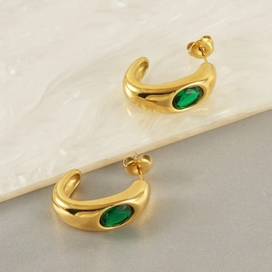 Polished gold C-shaped hoop earrings with green oval zircon on marble background