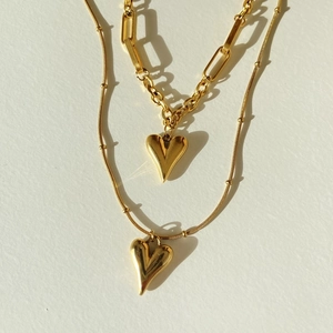 Detail of layered gold-plated heart pendant necklaces with toggle clasp and paperclip chain