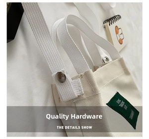 Detail of metal snap button and green woven label on a cream canvas bucket bag