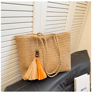Close-up of woven straw tote bag featuring decorative orange tassels and wood beads