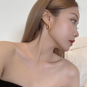 Close-up of golden irregular wavy textured hoop earrings on a model's ear
