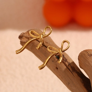 Macro shot of gold bow stud earrings on a wood stand with a warm blurred background