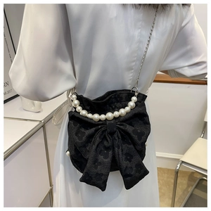 Detail of black bow crossbody bag with floral texture and pearl handle worn by a model