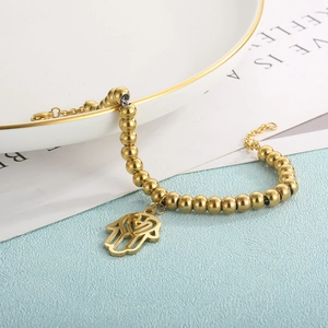 Detail of golden beaded bracelet featuring a Hamsa Hand charm on a marble background