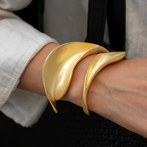 Detail of matte gold leaf cuff bracelet with brushed metal texture worn by a model