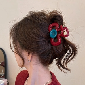 Red bow-shaped hair claw clip with blue button detail worn on model for hair styling