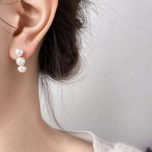 Close-up of elegant vertical three-pearl drop earrings on model with gold finish