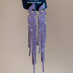 Macro shot of long purple rhinestone tassel earrings with a sparkling wave-shaped base