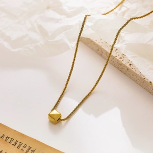 Close-up of golden stainless steel chain with cube pendant on textured stone background