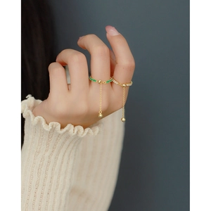 Detailed view of adjustable gold rings with green gemstone and chain tassel on hand