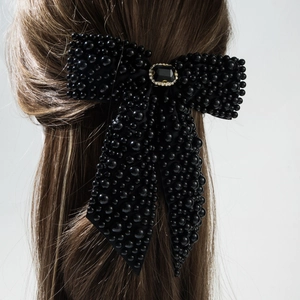 Detail of a black pearl bow hair clip with a centered black gemstone and sparkling rhinestones
