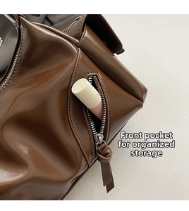 Detail of dark brown leather crossbody bag featuring front zipper pocket and knotted puller