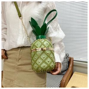 Detail of creative pineapple-shaped crossbody bag with gold rivets and green leaf handle