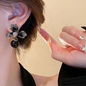 Exaggerated asymmetrical crystal flower earrings with black pearls worn by a model