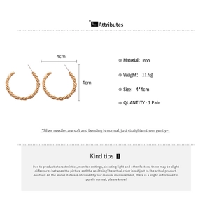 Macro view of gold twisted C-hoop earrings with 4cm diameter and detailed iron texture