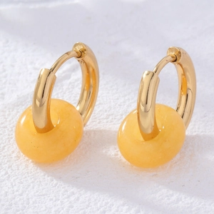 Detail of doughnut-shaped amber stone earrings with gold hoops on white stone background