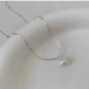 Detailed view of a Baroque pearl pendant on a silver-tone chain over a ceramic bowl
