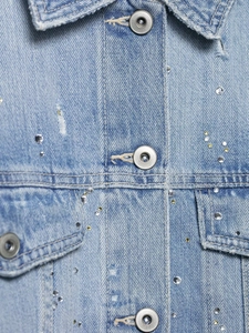 Gros plan sur une veste en jean bleu clair avec des strass et des boutons en métal