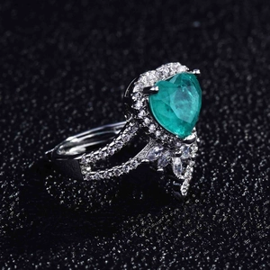 Macro shot of heart-shaped green gemstone ring with pavé diamond halo on black background