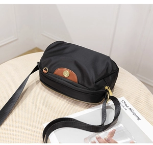 Detail of black oxford fabric crossbody bag with brown leather accent and golden metal logo