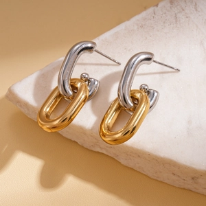 Detail of geometric oval earrings in gold and silver finish on white marble surface