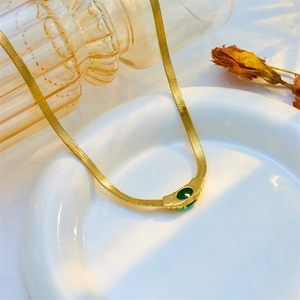 Retro gold snake chain necklace featuring a vintage oval green gemstone on a white plate
