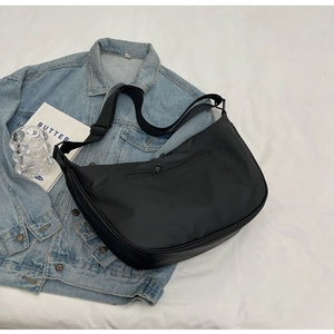 Detail of minimalist black nylon crescent bag styled on casual denim jacket back