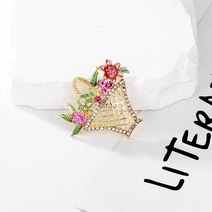Hollow flower basket brooch with pink crystals and green enamel on a white stone base