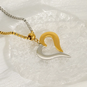 Two-tone stainless steel heart pendant on box chain necklace over textured glass