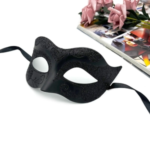 Detail of black glitter masquerade mask with ornate scroll patterns and silk ribbons