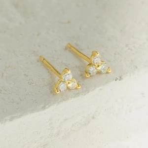 Gros plan de boucles d'oreilles triangle dorées avec trois zircons sur socle en pierre
